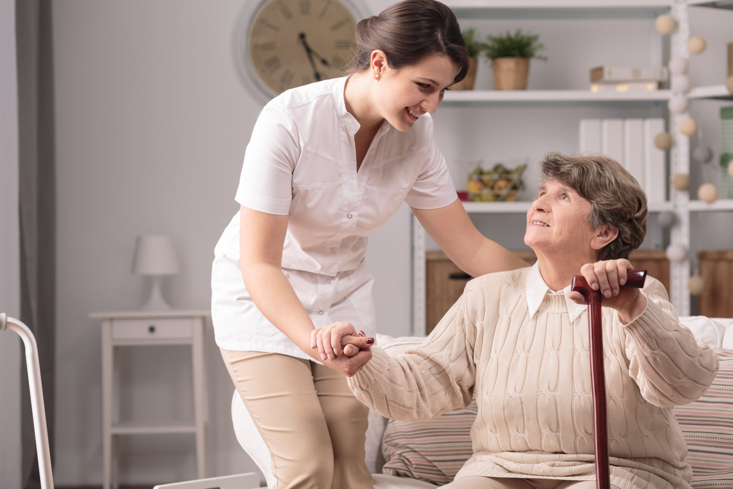 A caregiver assists an elderly woman in a cozy room, promoting a warm, supportive atmosphere focused on companionship and care.